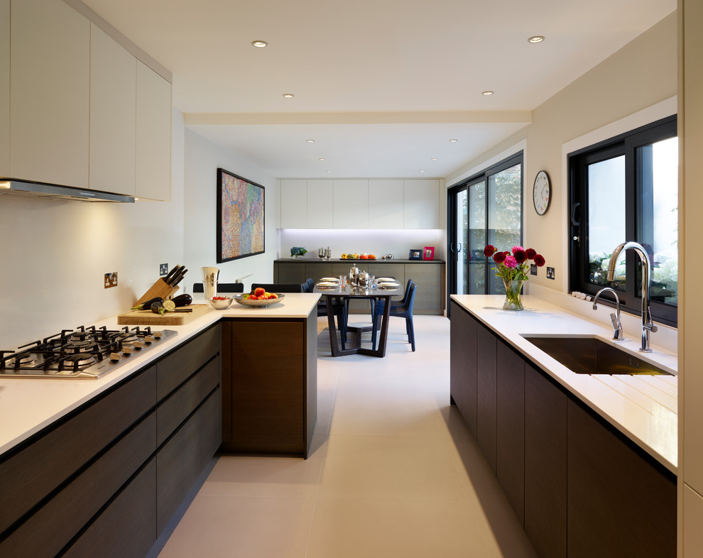 Photo of a contemporary galley kitchen in London with an undermount sink, flat-panel cabinets, dark wood cabinets, white splashback, stainless steel appliances and beige floor.