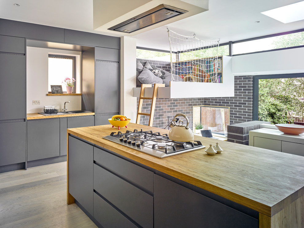 Design ideas for a mid-sized contemporary kitchen in London with flat-panel cabinets, grey cabinets, wood benchtops, light hardwood floors, with island and grey floor.