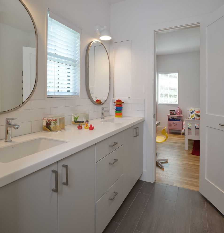 Mid-sized modern kids bathroom in Houston with flat-panel cabinets, grey cabinets, an alcove tub, a shower/bathtub combo, a two-piece toilet, white tile, ceramic tile, white walls, porcelain floors, an undermount sink, solid surface benchtops, brown floor and a shower curtain.