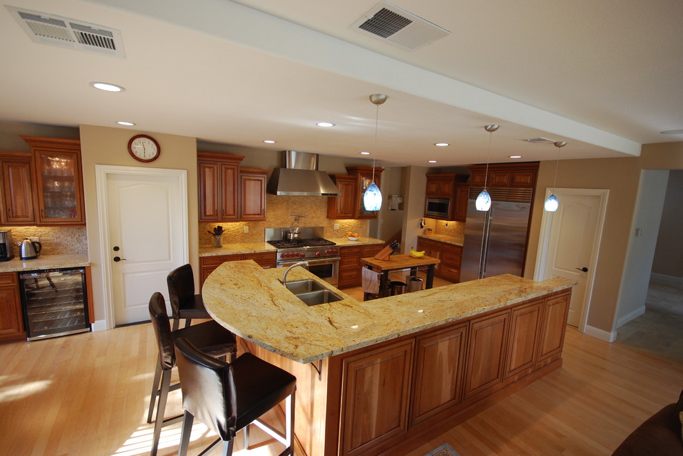 This is an example of a large traditional eat-in kitchen in Sacramento with an undermount sink, raised-panel cabinets, medium wood cabinets, granite benchtops, beige splashback, stone tile splashback, stainless steel appliances, light hardwood floors and with island.