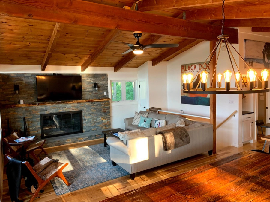 Exemple d'un salon montagne ouvert avec un sol en bois brun, une cheminée standard, un manteau de cheminée en pierre, un téléviseur fixé au mur et un plafond en bois.