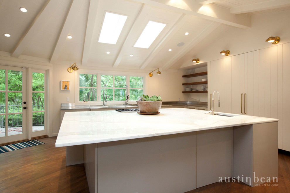 Inspiration for a large transitional u-shaped medium tone wood floor eat-in kitchen remodel with an integrated sink, flat-panel cabinets, white cabinets, stainless steel countertops, white backsplash, stone slab backsplash, stainless steel appliances and white walls