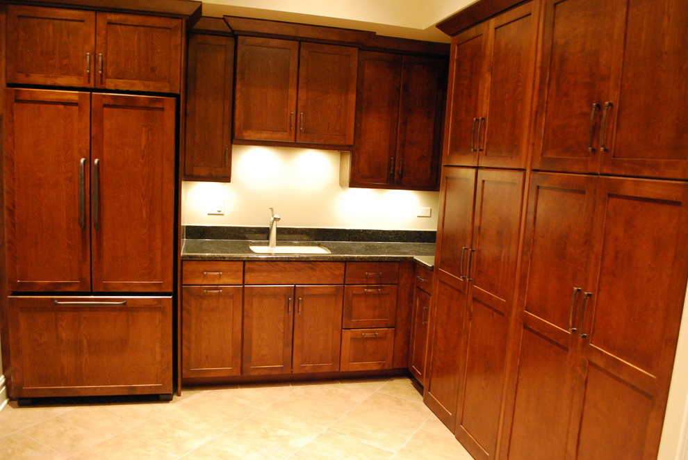 Photo of an expansive transitional l-shaped utility room in Chicago with an undermount sink, shaker cabinets, granite benchtops, ceramic floors, a concealed washer and dryer, beige walls and dark wood cabinets.