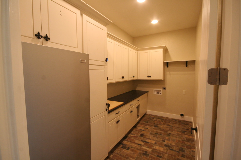 Inspiration for a small traditional galley dedicated laundry room in Austin with raised-panel cabinets, white cabinets, granite benchtops, beige walls, brick floors, a side-by-side washer and dryer, multi-coloured floor and black benchtop.