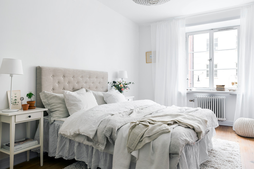 Photo of a mid-sized scandinavian master bedroom in Stockholm with white walls, light hardwood floors and no fireplace.