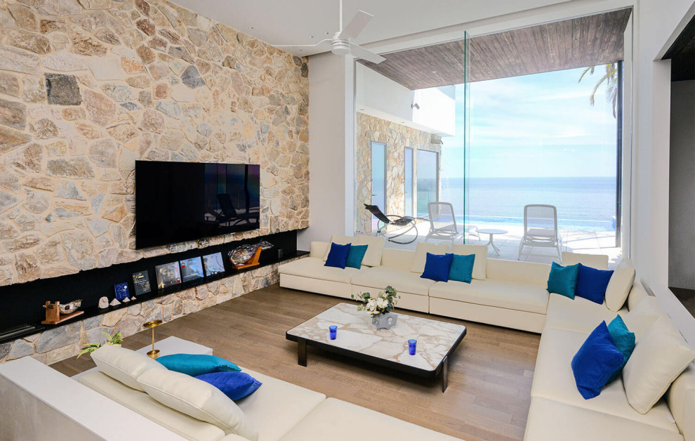 This is an example of a beach style enclosed living room with white walls, medium hardwood floors, a ribbon fireplace, a tile fireplace surround, a wall-mounted tv, beige floor and wallpaper.