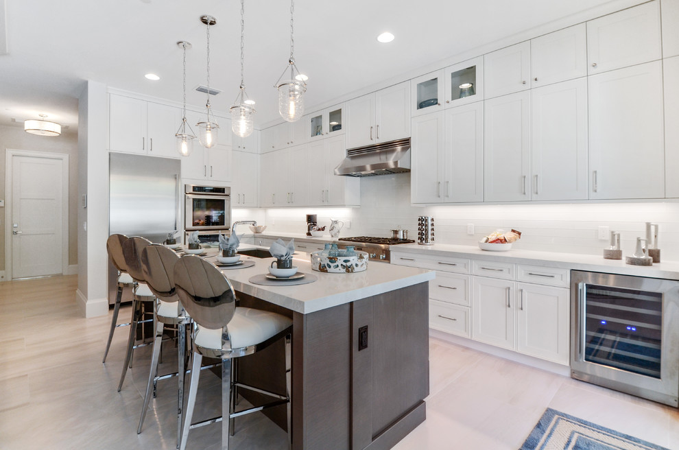 Photo of a large transitional l-shaped kitchen in Miami with shaker cabinets, white cabinets, white splashback, stainless steel appliances, with island and beige floor.