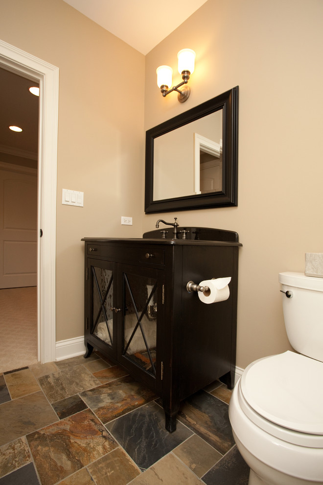 Small traditional powder room in Chicago with glass-front cabinets, dark wood cabinets, a two-piece toilet, beige walls, slate floors and brown tile.