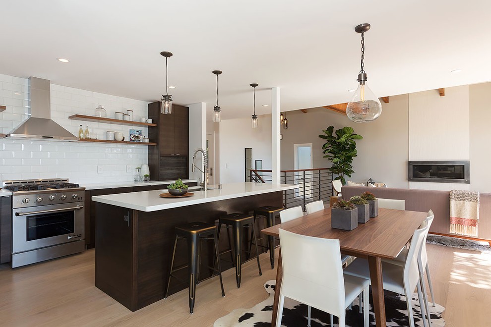 Photo of a contemporary open plan kitchen in San Francisco with a single-bowl sink, flat-panel cabinets, dark wood cabinets, quartz benchtops, white splashback, subway tile splashback, stainless steel appliances, light hardwood floors and with island.