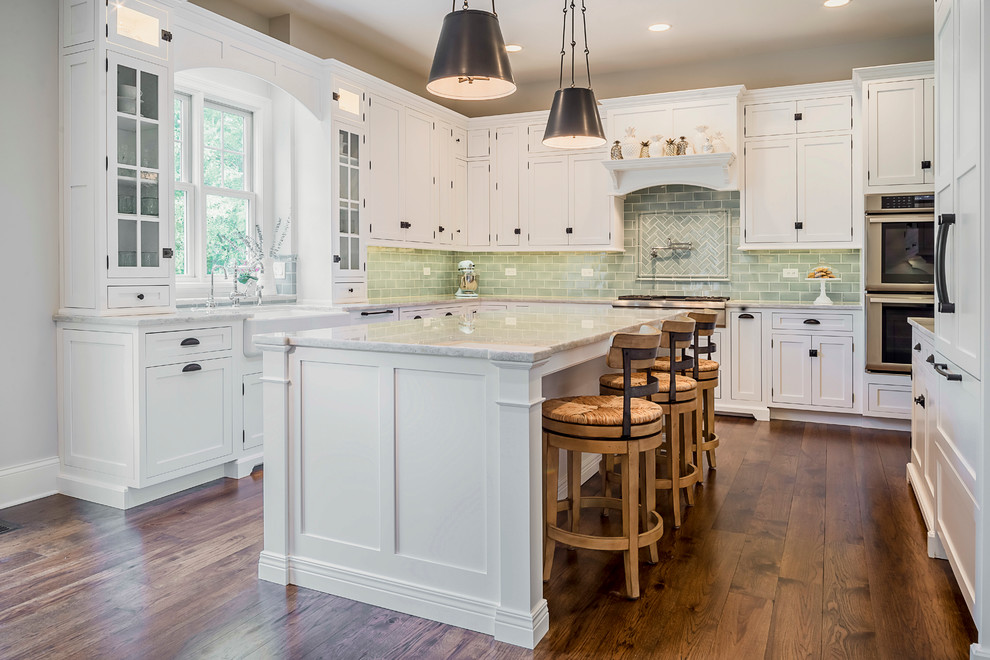 Example of a large transitional u-shaped medium tone wood floor eat-in kitchen design in Chicago with a farmhouse sink, glass-front cabinets, white cabinets, terrazzo countertops, green backsplash, glass tile backsplash, colored appliances and an island