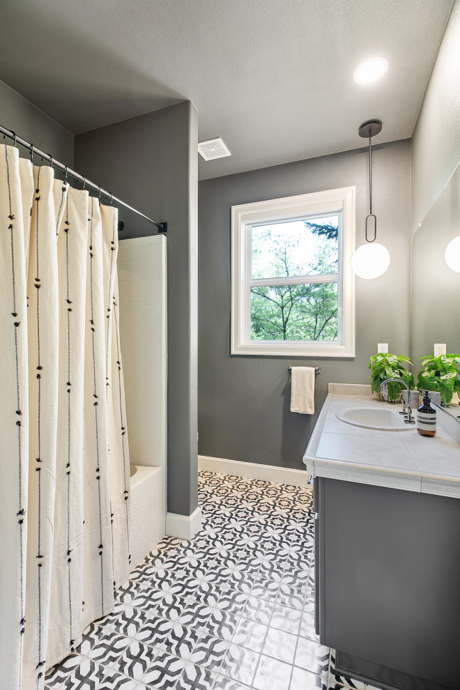 Photo of a mid-sized eclectic 3/4 bathroom in Portland with raised-panel cabinets, black cabinets, a shower/bathtub combo, a one-piece toilet, black walls, ceramic floors, a drop-in sink, tile benchtops, black floor, a shower curtain, beige benchtops, a single vanity and a built-in vanity.