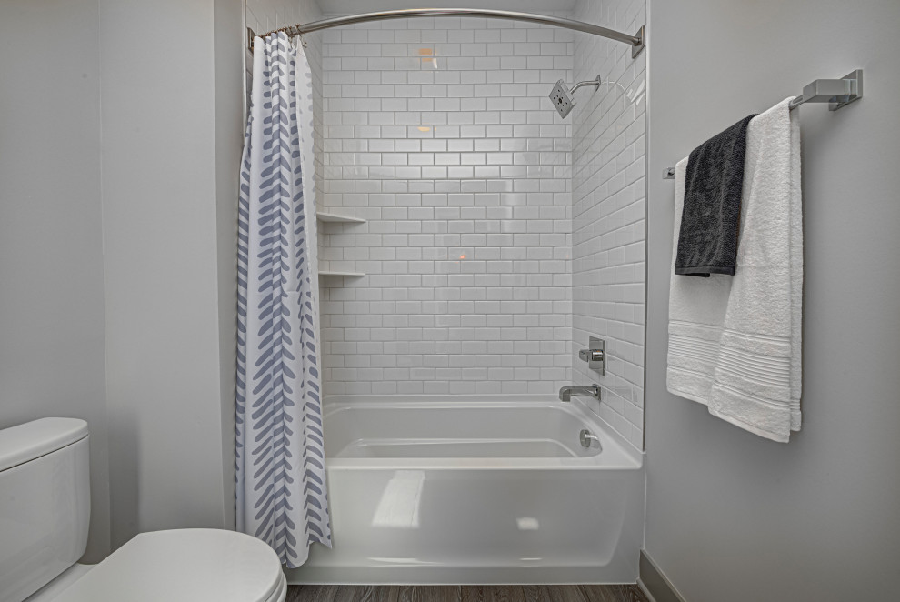 Inspiration pour une salle de bain principale design de taille moyenne avec une baignoire d'angle, un combiné douche/baignoire, WC à poser, un mur gris, une cabine de douche avec un rideau, un carrelage blanc, un carrelage métro, un sol en bois brun, un sol marron et des toilettes cachées.