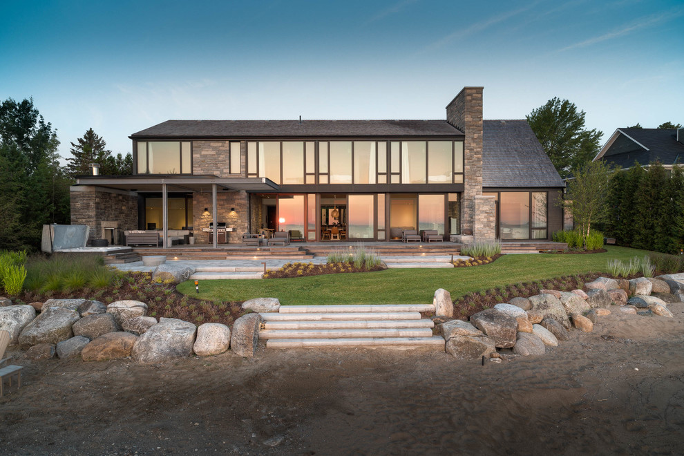 Beach style two-storey brown house exterior in Toronto with stone veneer, a hip roof and a shingle roof.