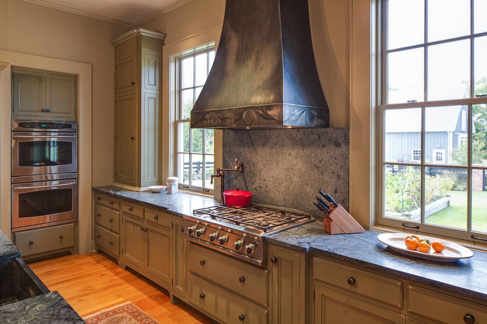 Inspiration for a large traditional kitchen in Nashville with a farmhouse sink, recessed-panel cabinets, brown cabinets, soapstone benchtops, grey splashback, window splashback, stainless steel appliances, medium hardwood floors, with island and brown floor.