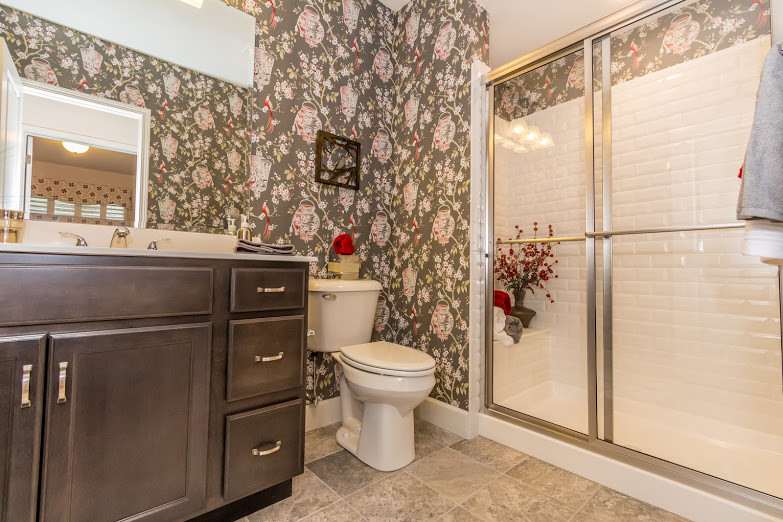 Inspiration for a transitional master white tile and subway tile ceramic tile and gray floor doorless shower remodel with recessed-panel cabinets, dark wood cabinets, a one-piece toilet, multicolored walls, an integrated sink and solid surface countertops