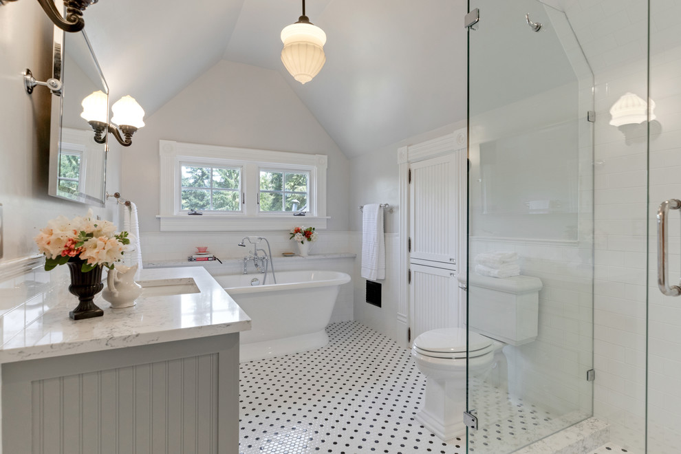 Traditional master bathroom in Portland with grey cabinets, a freestanding tub, a two-piece toilet, white tile, subway tile, grey walls, ceramic floors, an undermount sink, engineered quartz benchtops, multi-coloured floor, a hinged shower door and white benchtops.