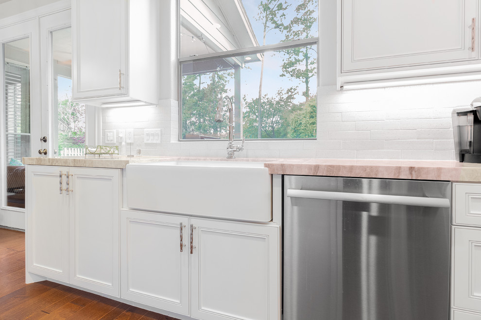 Mid-sized transitional l-shaped light wood floor and orange floor eat-in kitchen photo in Houston with a farmhouse sink, recessed-panel cabinets, white cabinets, quartzite countertops, white backsplash, subway tile backsplash, stainless steel appliances, an island and multicolored countertops