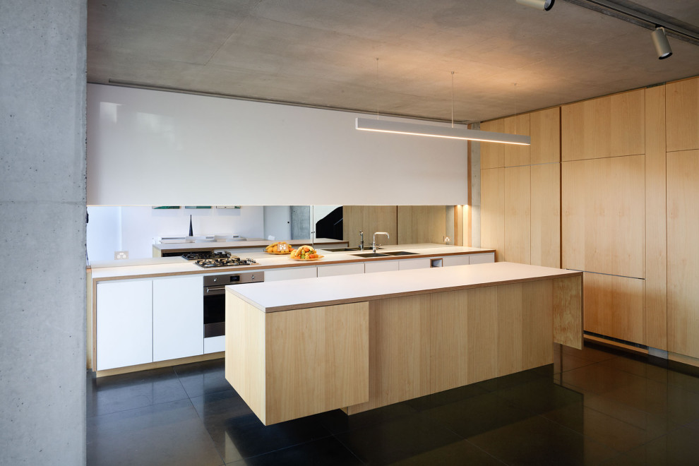 Photo of a large modern galley eat-in kitchen in Sydney with an undermount sink, light wood cabinets, laminate benchtops, mirror splashback, stainless steel appliances, with island, black floor and white benchtop.