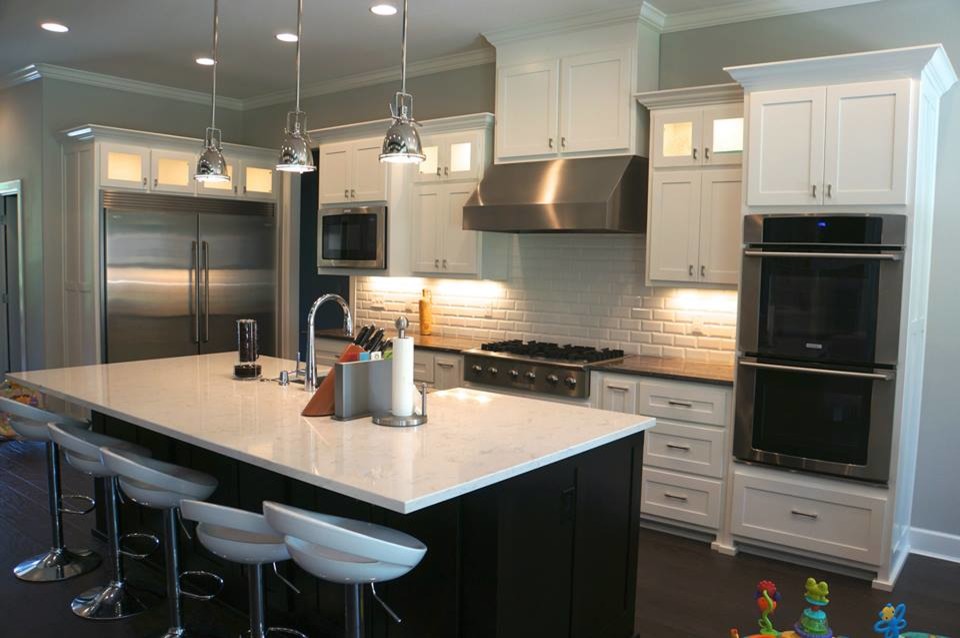 Mid-sized transitional dark wood floor eat-in kitchen photo with a farmhouse sink, recessed-panel cabinets, white cabinets, quartz countertops, white backsplash, ceramic backsplash, stainless steel appliances and an island