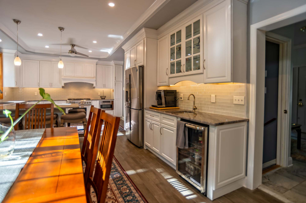 This is an example of a large traditional u-shaped eat-in kitchen in Philadelphia with an undermount sink, raised-panel cabinets, white cabinets, quartz benchtops, white splashback, glass tile splashback, stainless steel appliances, medium hardwood floors, a peninsula, brown floor and brown benchtop.