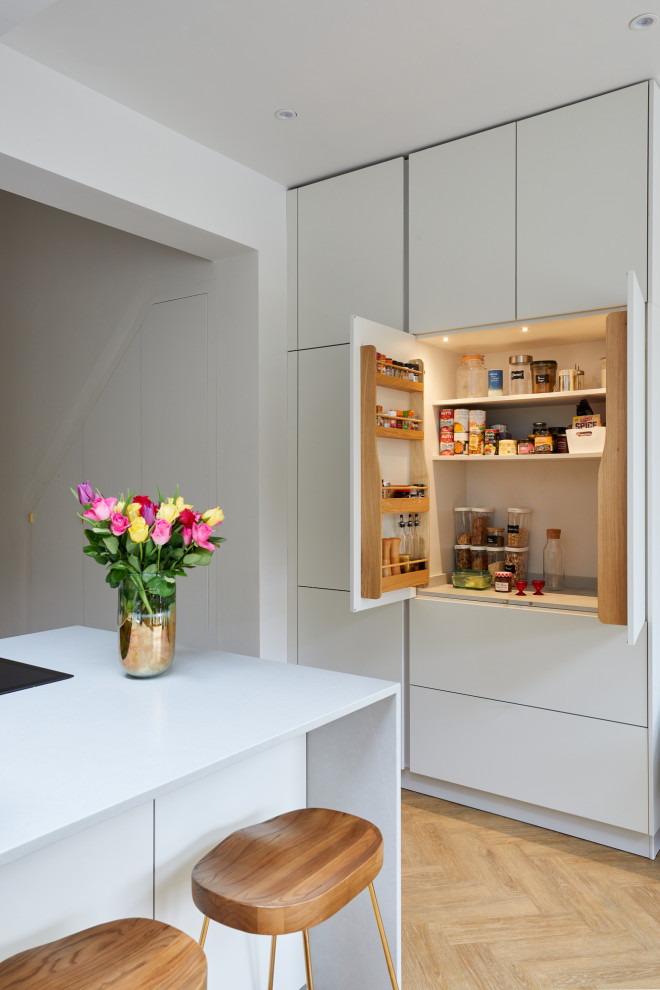This is an example of a small modern u-shaped kitchen/diner in London with a submerged sink, flat-panel cabinets, white cabinets, engineered stone countertops, yellow splashback, glass sheet splashback, stainless steel appliances, medium hardwood flooring, a breakfast bar, brown floors and white worktops.