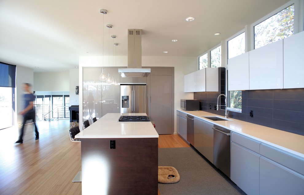 This is an example of a large modern l-shaped open plan kitchen in Seattle with an undermount sink, flat-panel cabinets, beige cabinets, quartz benchtops, black splashback, porcelain splashback, stainless steel appliances, bamboo floors and with island.