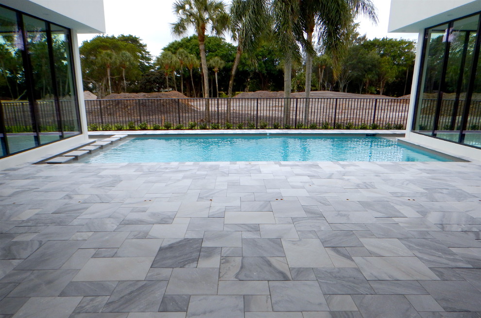 Photo of a large modern backyard rectangular lap pool in Tampa with natural stone pavers.