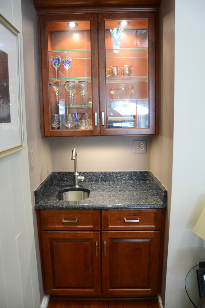 Photo of a small traditional single-wall wet bar in DC Metro with an undermount sink, raised-panel cabinets, medium wood cabinets, granite benchtops, medium hardwood floors, brown floor and blue benchtop.