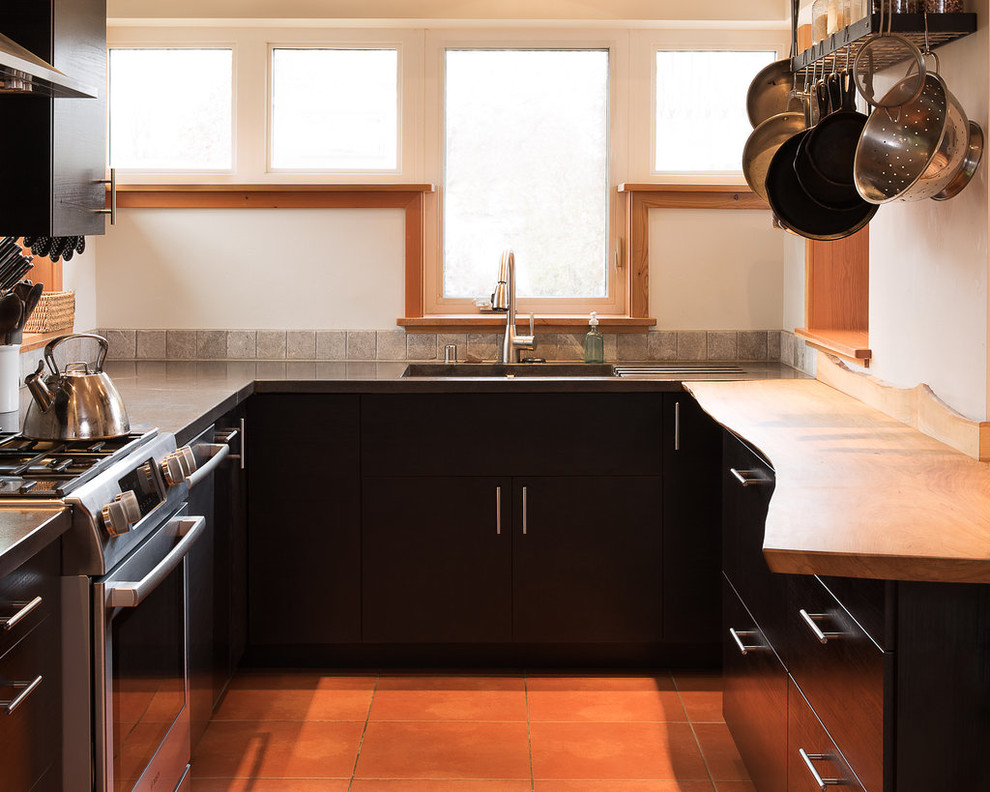 This is an example of a small contemporary galley open plan kitchen in Other with an undermount sink, flat-panel cabinets, black cabinets, concrete benchtops, grey splashback, stone tile splashback, stainless steel appliances, terra-cotta floors and a peninsula.