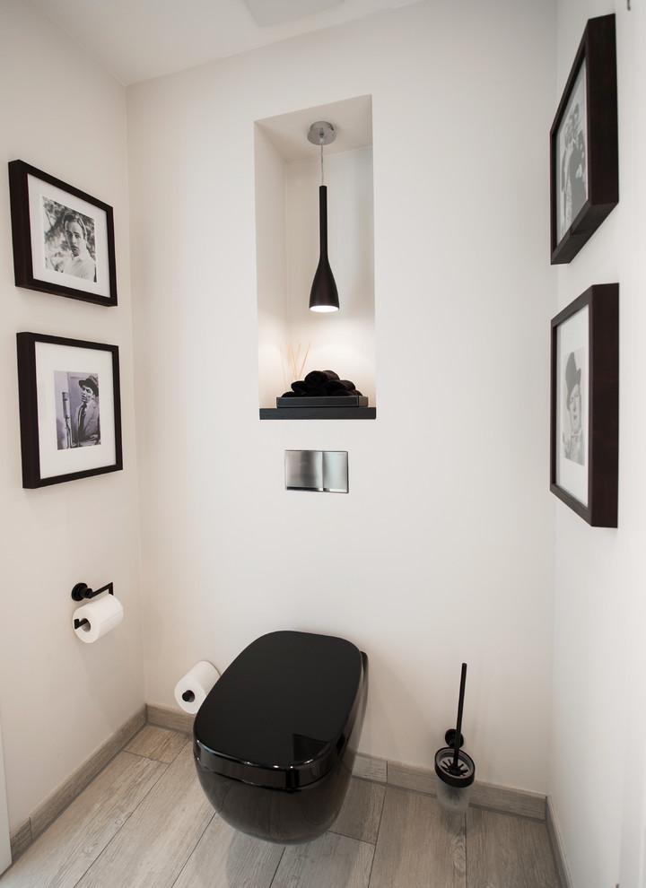 This is an example of a small contemporary powder room in Dortmund with a wall-mount toilet, white walls and medium hardwood floors.