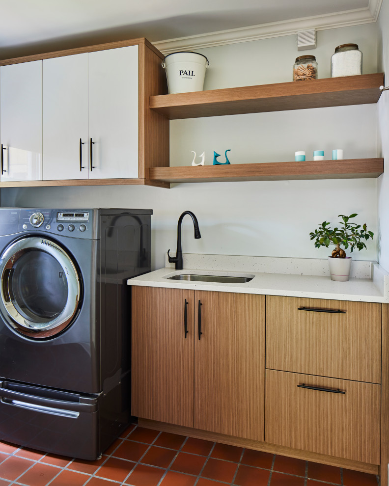 バーミングハムにあるお手頃価格の中くらいなミッドセンチュリースタイルのおしゃれなランドリールーム (I型、アンダーカウンターシンク、フラットパネル扉のキャビネット、白いキャビネット、白いキッチンパネル、赤い壁、テラコッタタイルの床、左右配置の洗濯機・乾燥機、白いキッチンカウンター) の写真