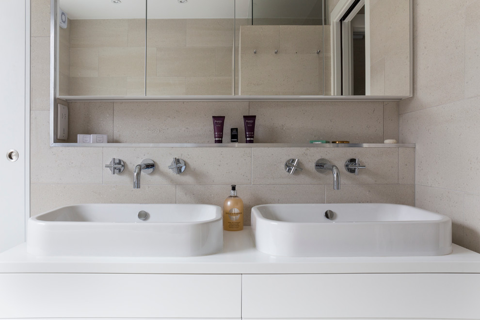 Photo of a small contemporary kids bathroom in London with flat-panel cabinets, white cabinets, a drop-in tub, an open shower, a wall-mount toilet, beige tile, porcelain tile, beige walls, porcelain floors, a drop-in sink, quartzite benchtops, beige floor and a sliding shower screen.