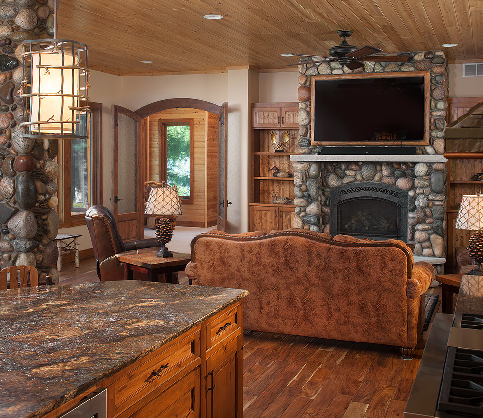 Design ideas for a mid-sized country open concept family room in Grand Rapids with beige walls, light hardwood floors, a standard fireplace, a stone fireplace surround and a wall-mounted tv.