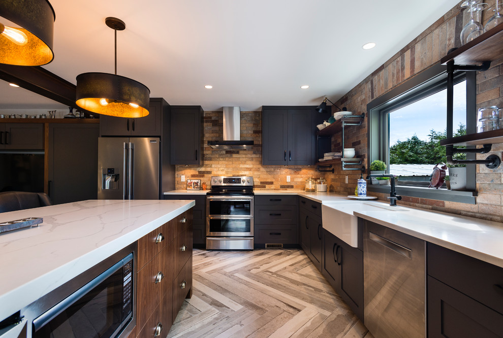Photo of a large industrial l-shaped open plan kitchen in Vancouver with an undermount sink, shaker cabinets, grey cabinets, quartz benchtops, brown splashback, brick splashback, stainless steel appliances, porcelain floors, with island and beige floor.