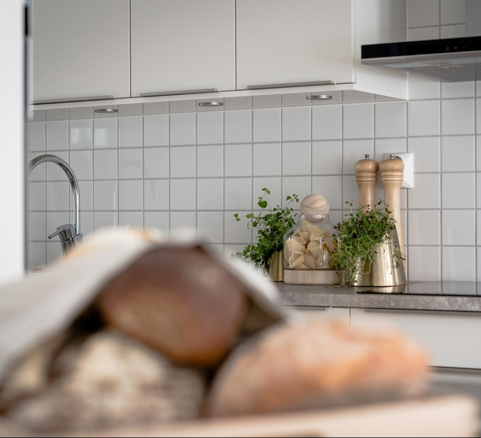Scandinavian galley eat-in kitchen in Stockholm with a double-bowl sink, flat-panel cabinets, white cabinets, white splashback, porcelain splashback, laminate floors and grey benchtop.