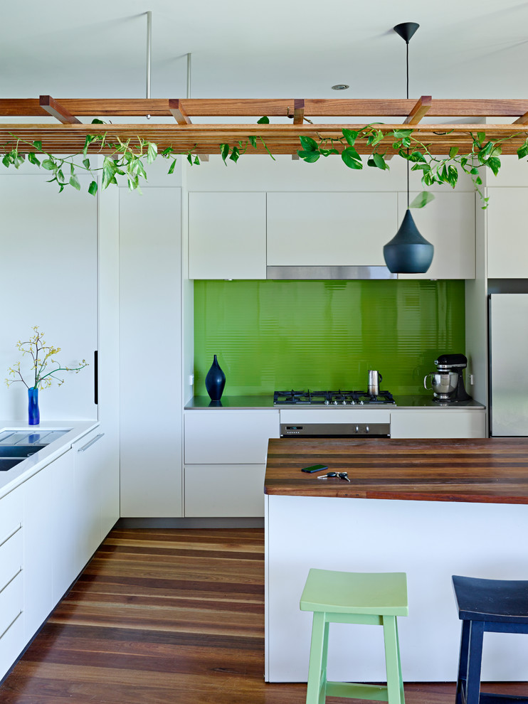 Design ideas for a mid-sized contemporary kitchen in Sunshine Coast with flat-panel cabinets, white cabinets, green splashback, glass tile splashback, stainless steel appliances, medium hardwood floors and with island.