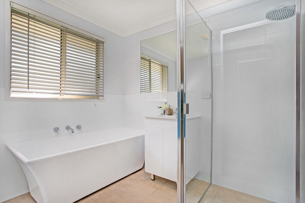 Photo of a small contemporary bathroom in Newcastle - Maitland with furniture-like cabinets, white cabinets, a freestanding tub, a corner shower, white tile, porcelain tile, white walls, ceramic floors, an integrated sink, beige floor and a hinged shower door.