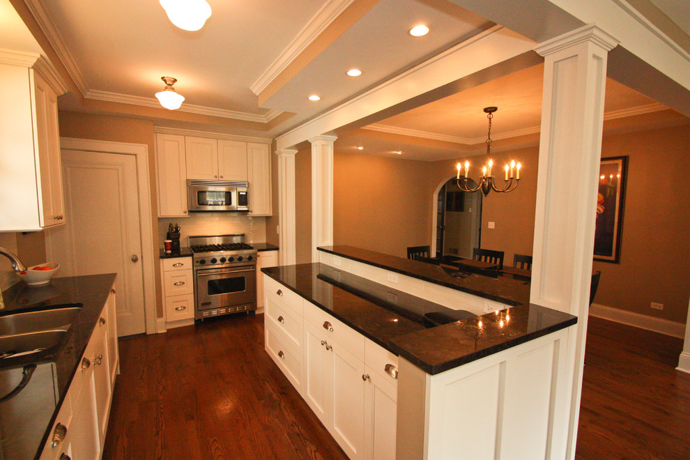 Enclosed kitchen - small transitional galley dark wood floor enclosed kitchen idea in Chicago with an undermount sink, beaded inset cabinets, white cabinets, granite countertops, white backsplash, porcelain backsplash, stainless steel appliances and an island
