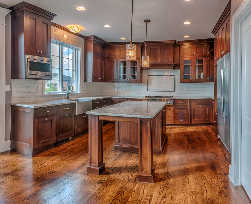 Eat-in kitchen - mid-sized transitional u-shaped dark wood floor eat-in kitchen idea in Chicago with a farmhouse sink, recessed-panel cabinets, medium tone wood cabinets, granite countertops, white backsplash, ceramic backsplash, stainless steel appliances and an island
