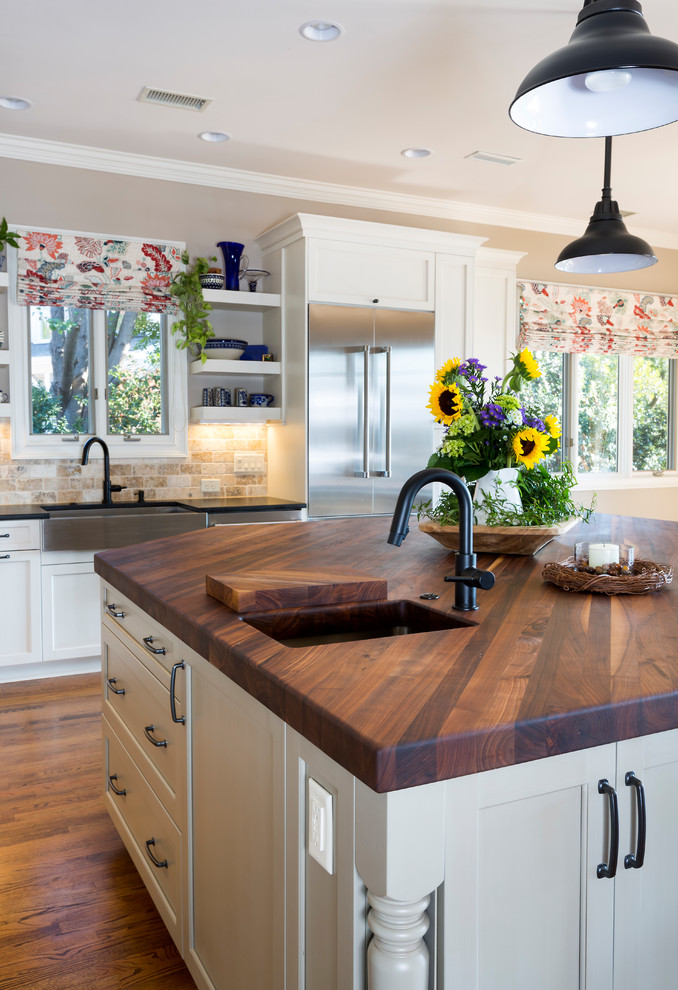 This is an example of a large country l-shaped open plan kitchen in Charlotte with an undermount sink, shaker cabinets, white cabinets, wood benchtops, multi-coloured splashback, stone tile splashback, stainless steel appliances, medium hardwood floors and with island.
