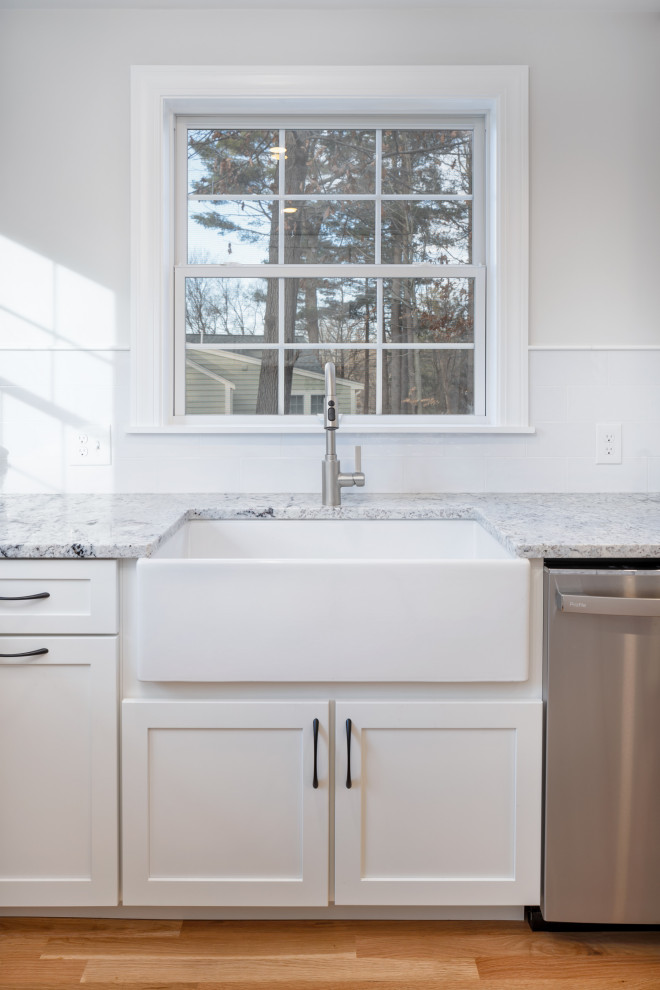 Eat-in kitchen - mid-sized transitional u-shaped medium tone wood floor eat-in kitchen idea in Boston with a farmhouse sink, shaker cabinets, white cabinets, granite countertops, white backsplash, subway tile backsplash, stainless steel appliances, a peninsula and multicolored countertops