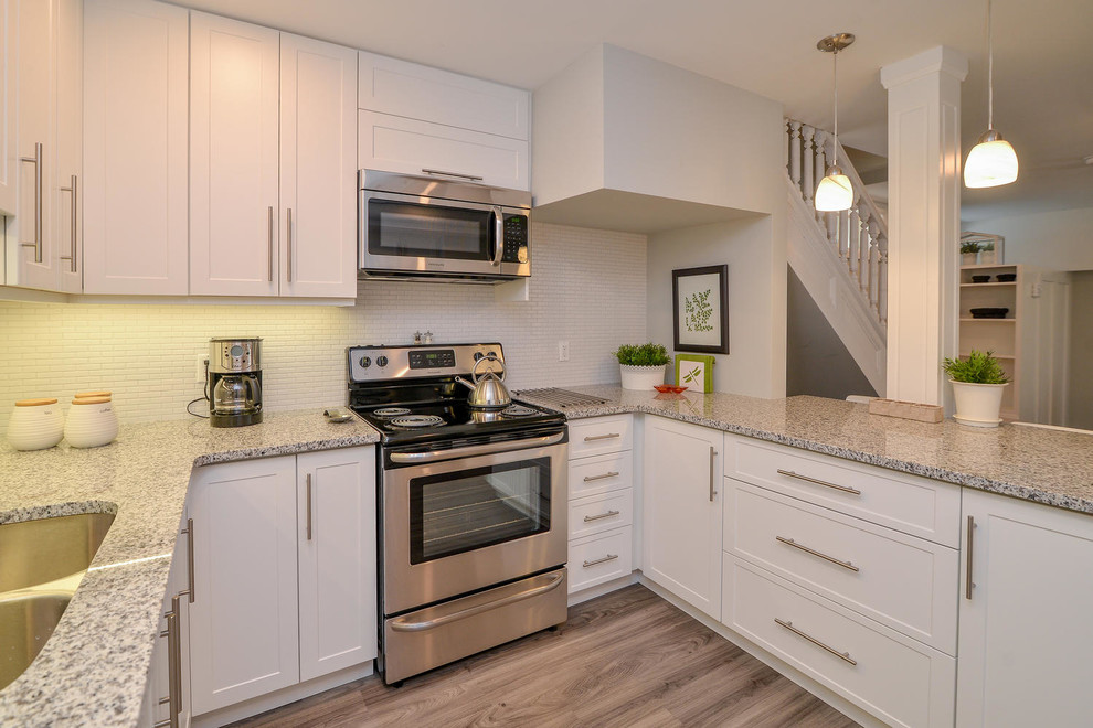 Example of a mid-sized transitional u-shaped medium tone wood floor and gray floor open concept kitchen design with an undermount sink, shaker cabinets, white cabinets, granite countertops, stainless steel appliances and a peninsula