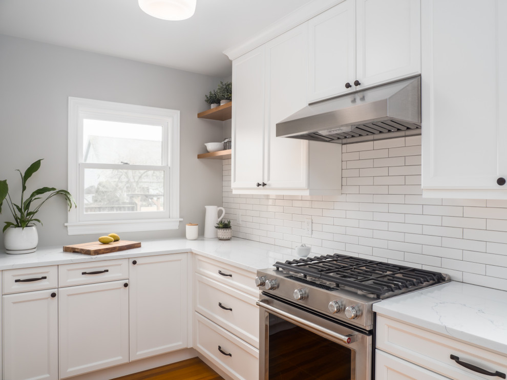 Example of a small transitional galley medium tone wood floor and brown floor enclosed kitchen design in Seattle with an undermount sink, recessed-panel cabinets, white cabinets, quartzite countertops, white backsplash, porcelain backsplash, stainless steel appliances, no island and white countertops