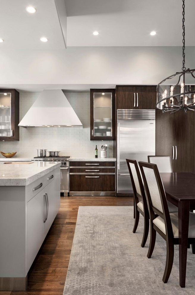 This is an example of a transitional kitchen in Denver with flat-panel cabinets, dark wood cabinets, white splashback, matchstick tile splashback, stainless steel appliances, dark hardwood floors and with island.