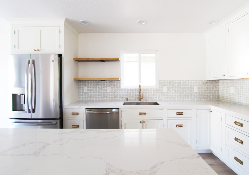 Mid-sized l-shaped light wood floor and brown floor open concept kitchen photo with an undermount sink, shaker cabinets, white cabinets, quartz countertops, gray backsplash, mosaic tile backsplash, stainless steel appliances, an island and white countertops