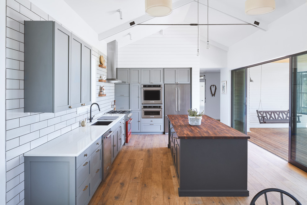 Scandinavian l-shaped kitchen in Austin with an undermount sink, recessed-panel cabinets, grey cabinets, wood benchtops, white splashback, stainless steel appliances, medium hardwood floors, with island, brown floor and brown benchtop.