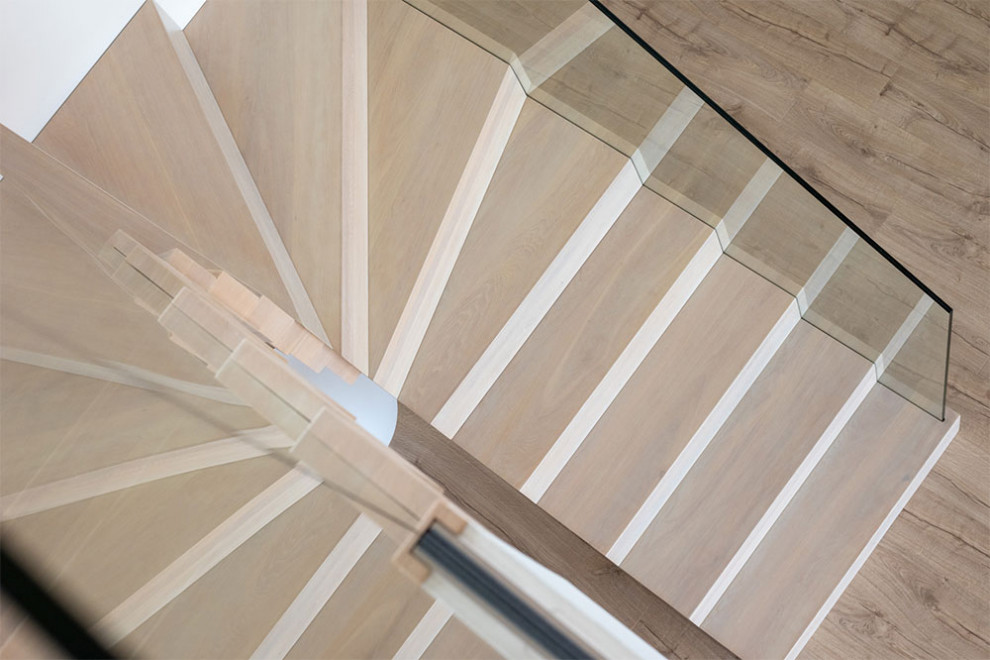 Imagen de escalera curva minimalista con escalones de vidrio, contrahuellas de madera y barandilla de vidrio
