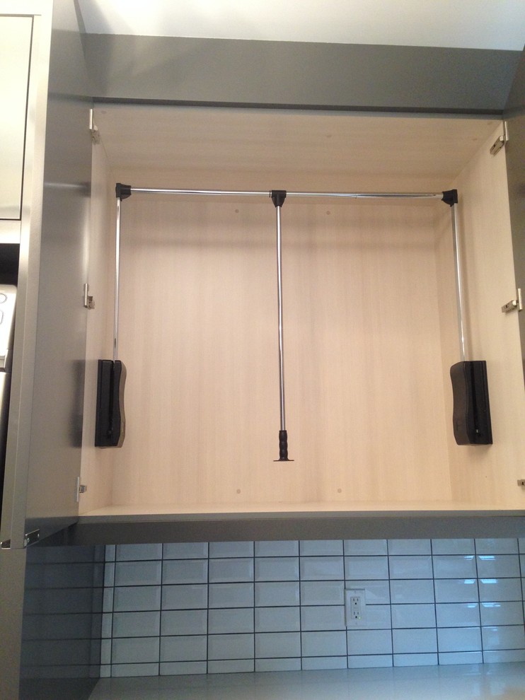 Example of a mid-sized l-shaped porcelain tile dedicated laundry room design in Calgary with an undermount sink, flat-panel cabinets, gray cabinets, quartz countertops, white walls and a stacked washer/dryer