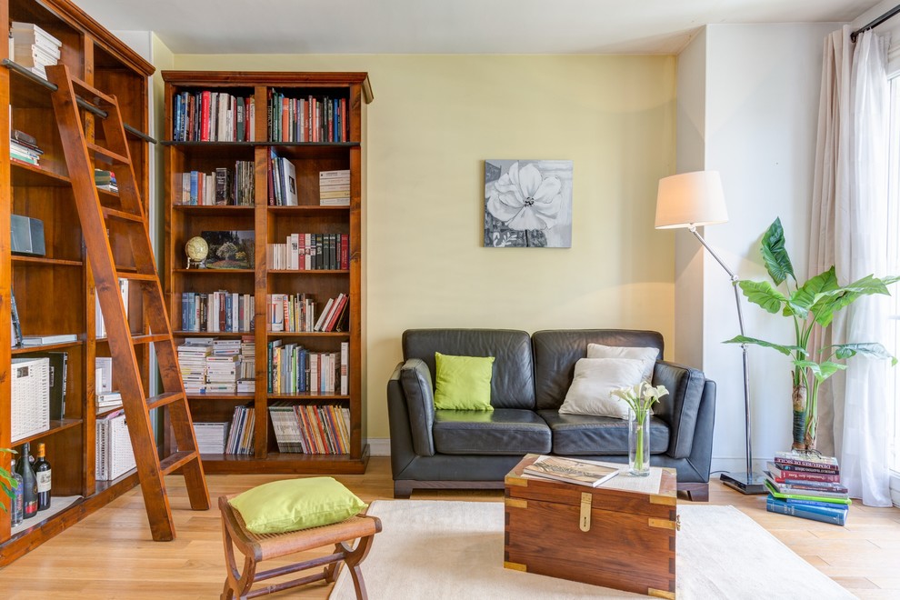 Mid-sized traditional enclosed living room in Paris with a library, yellow walls, light hardwood floors, no fireplace and no tv.