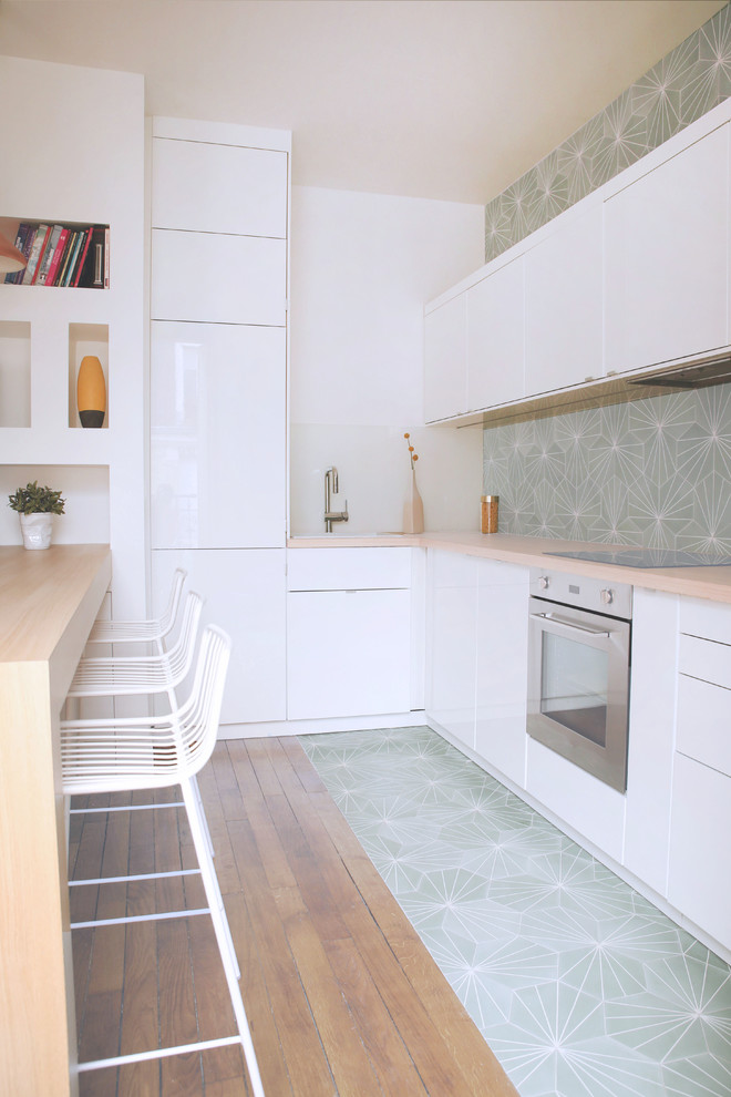 This is an example of a mid-sized contemporary l-shaped kitchen in Paris with white cabinets, wood benchtops, multi-coloured splashback, cement tile splashback, a peninsula, flat-panel cabinets and stainless steel appliances.